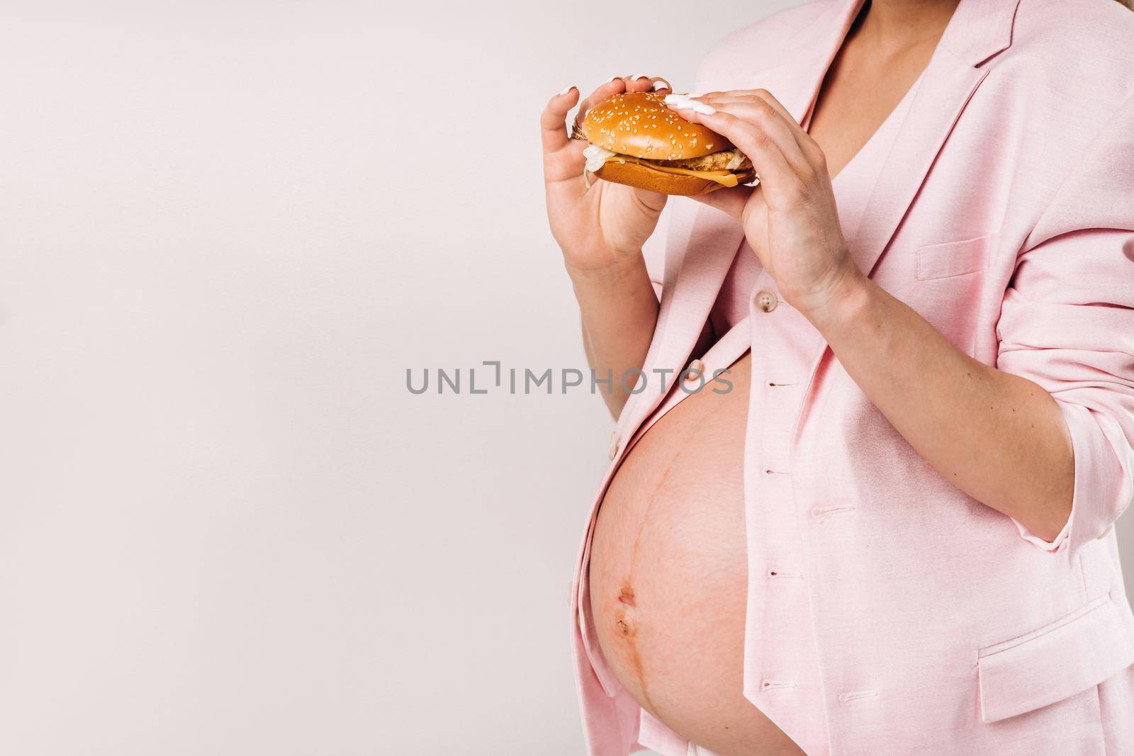Close-up of a pregnant girl in a suit with hamburgers in her hands on a gray background.