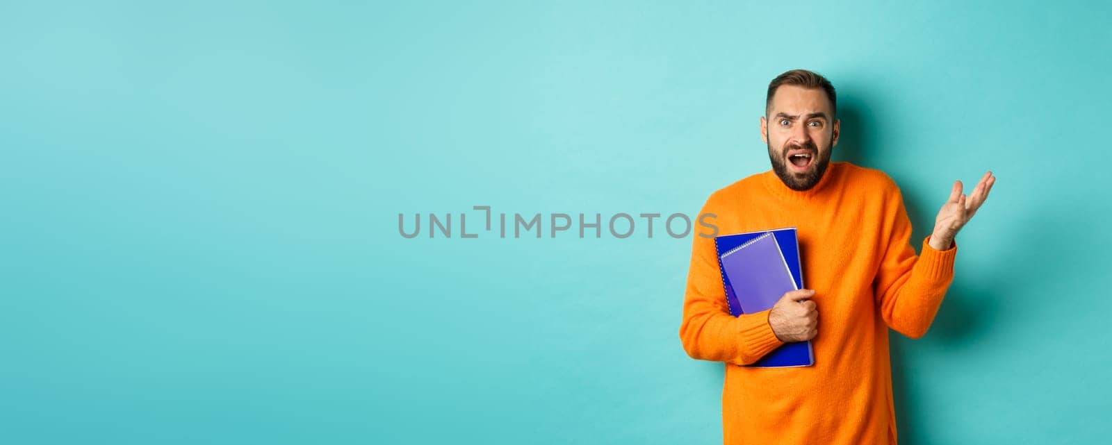 Education. Confused and disappointed man arguing, holding notebooks and complaining, standing over light blue background.