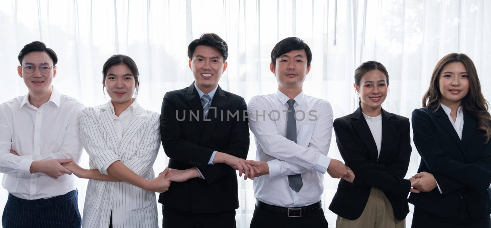 Cohesive group of businesspeople standing in row, holding hand in line together after meeting to promote harmony in workplace. Asian office workers strong teamwork and unity concept.