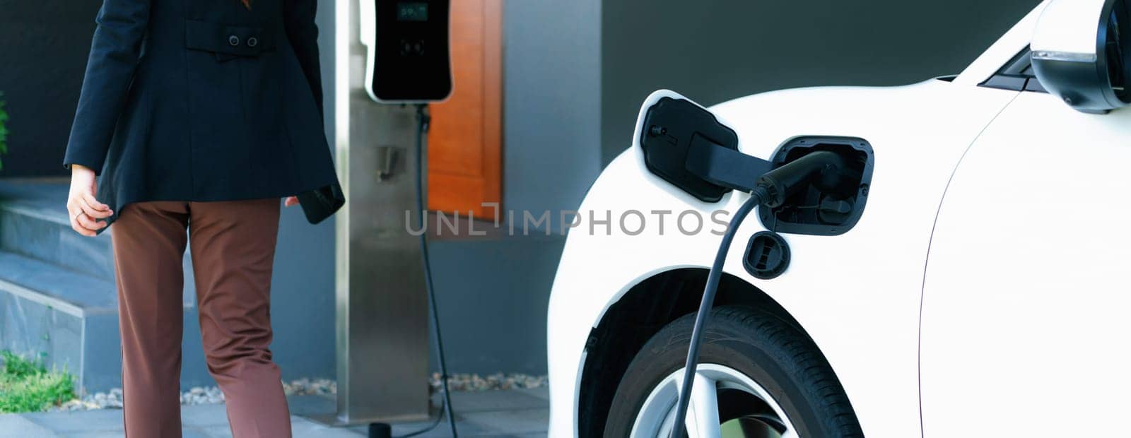 Progressive asian woman and electric car with home charging station. Concept of the use of electric vehicles in a progressive lifestyle contributes to a clean and healthy environment.