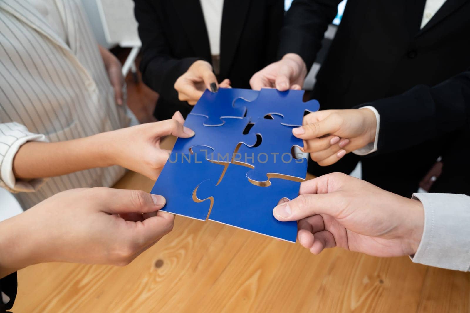 Closeup top view business team of office worker putting jigsaw puzzle together over table filled with financial report paper in workplace with manager to promote harmony concept in meeting room.