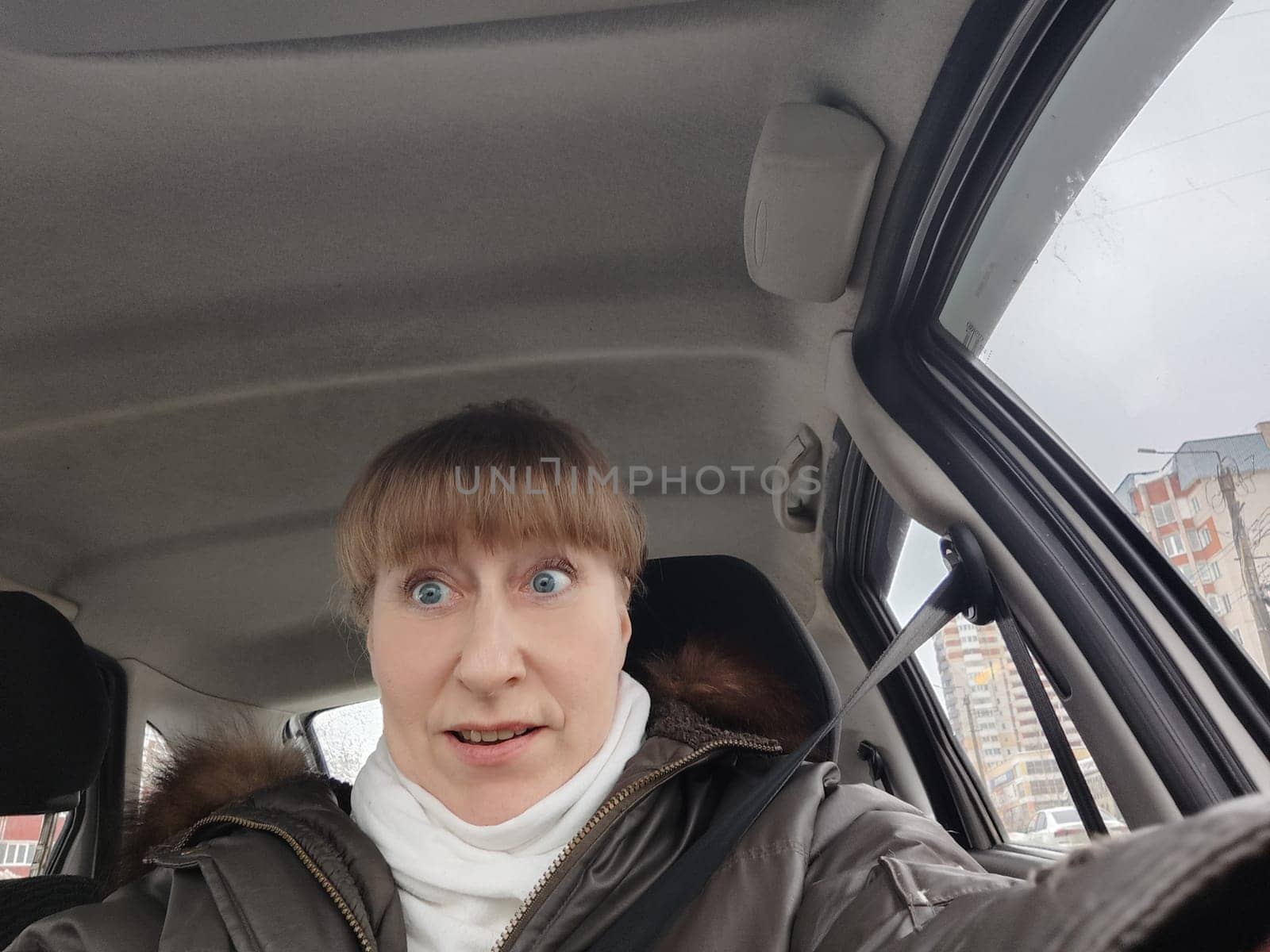 Portrait of adult cute funny blonde woman in warm clothes taking a selfie inside the car and driving it. The concept of a pleasant trip in spring, autumn, winter by keleny