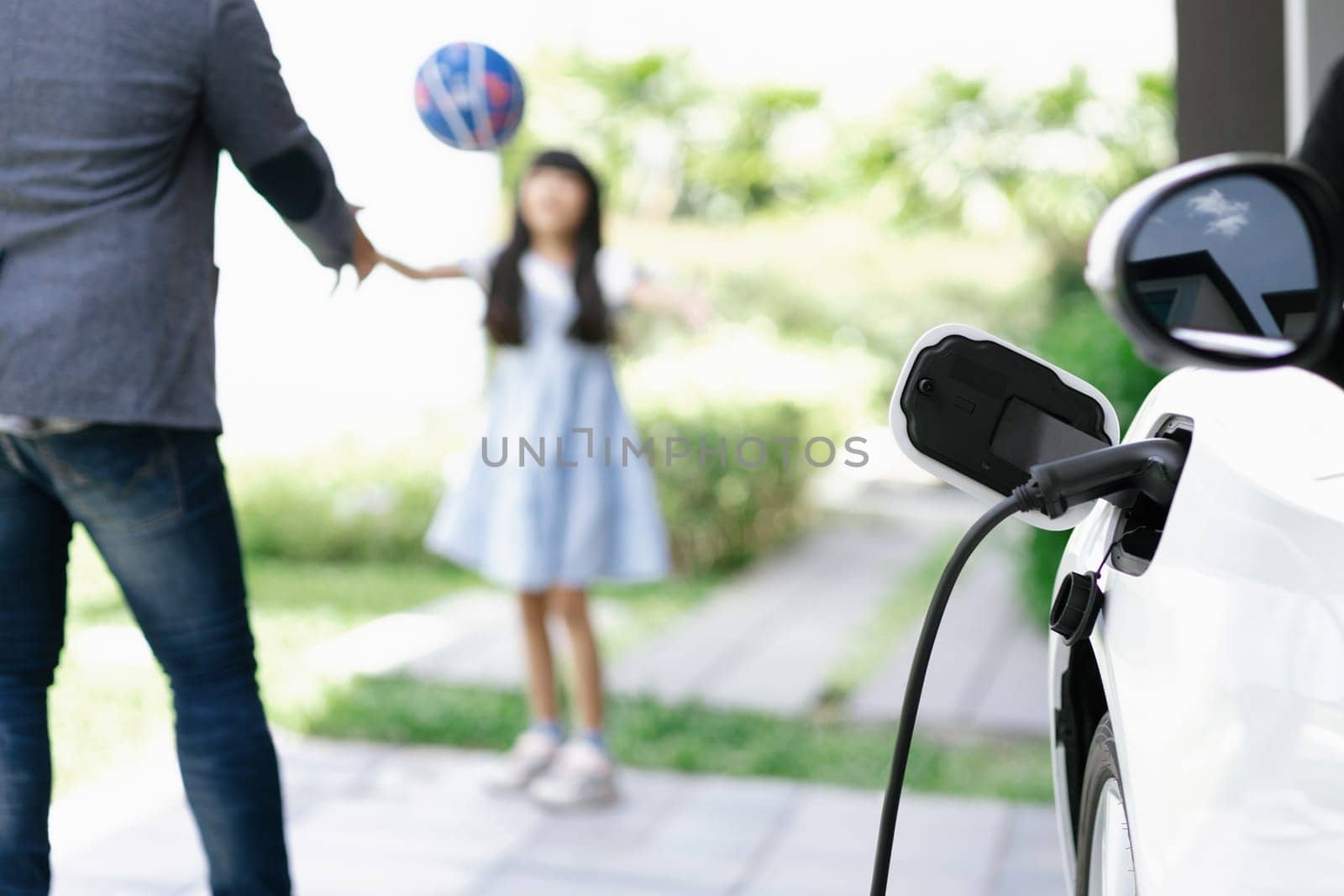 Progressive father and daughter plugs EV charger from home charging station to electric vehicle. Future eco-friendly car with EV cars powered by renewable source of clean energy.