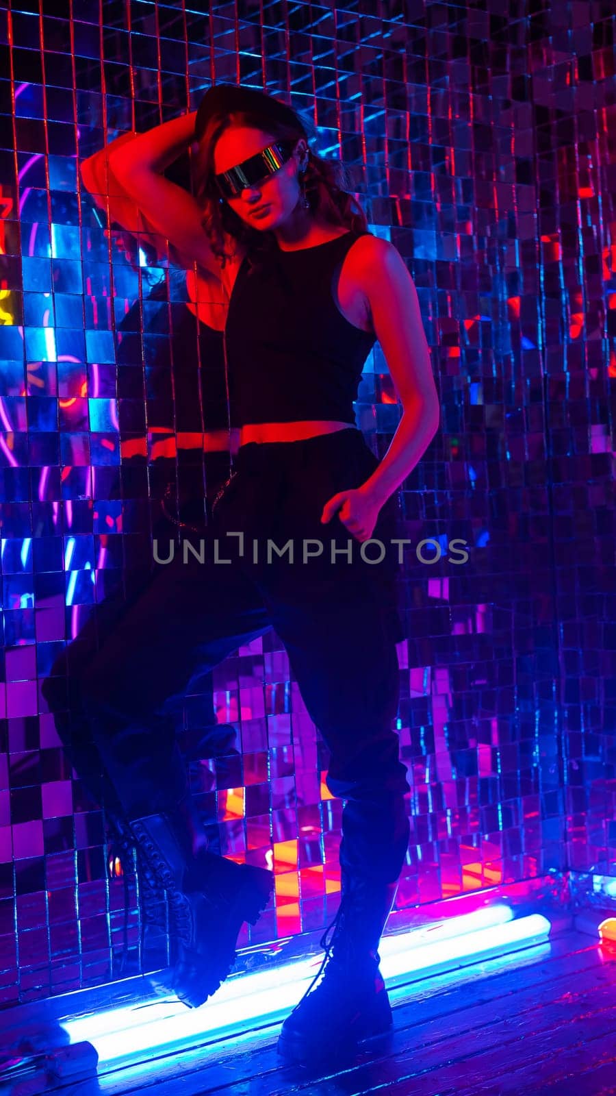 Portrait of a caucasian woman in sunglasses in neon light against a mirror wall