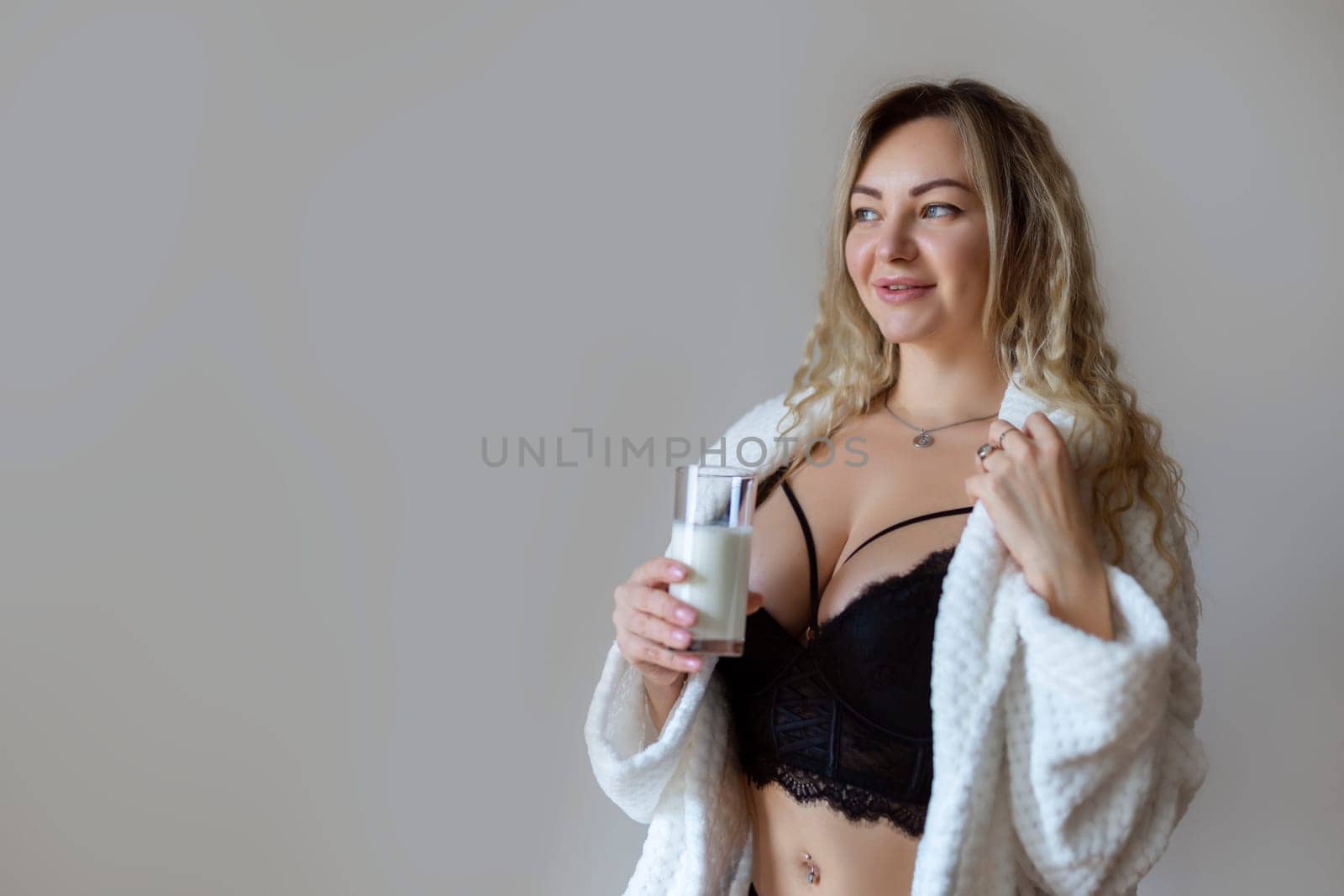 sexy young woman in black lingerie pouring milk on body isolated on grey.