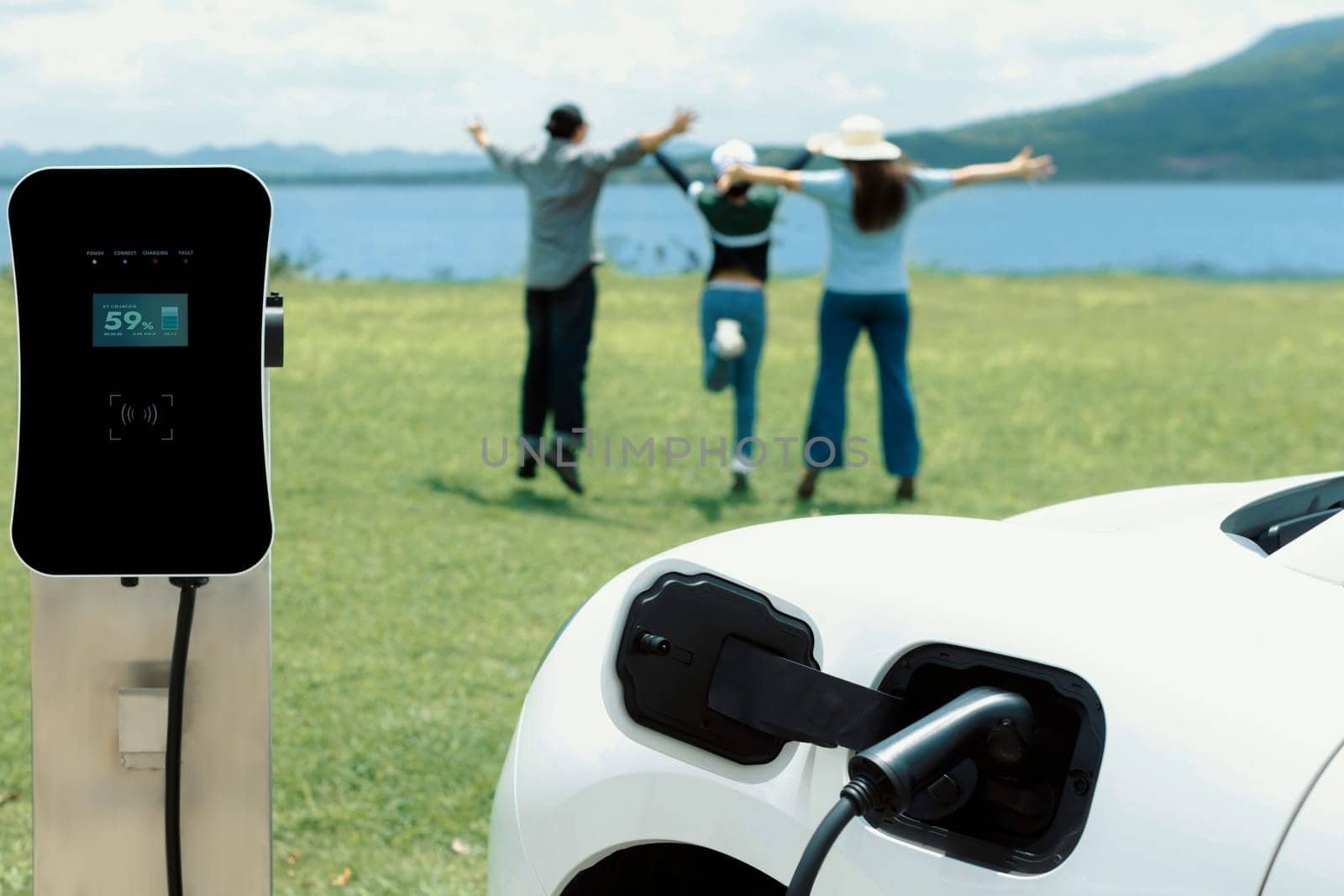 Concept of progressive happy family enjoying their time at green field and lake with electric vehicle. Electric vehicle driven by clean renewable from eco-friendly power sauce.