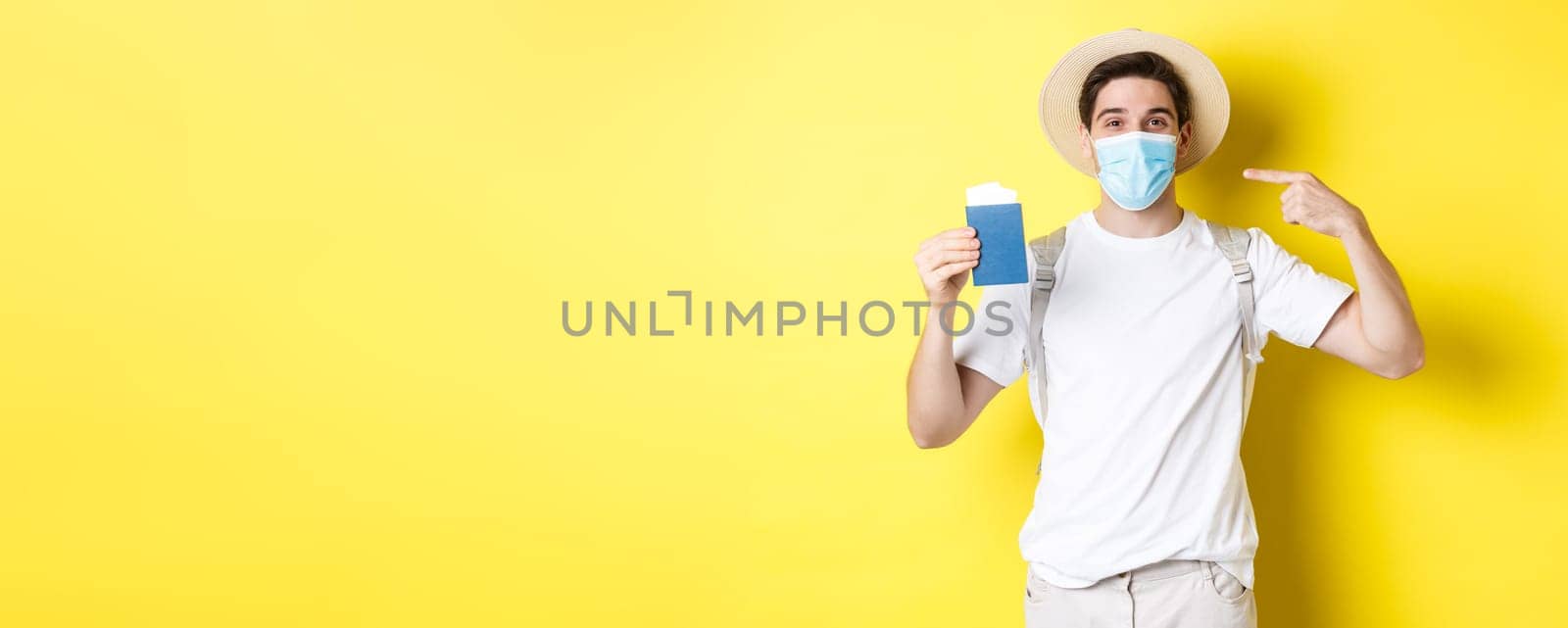 Concept of covid-19, tourism and pandemic. Man tourist showing passport, travelling in medical mask for protection from coronavirus, yellow background by Benzoix