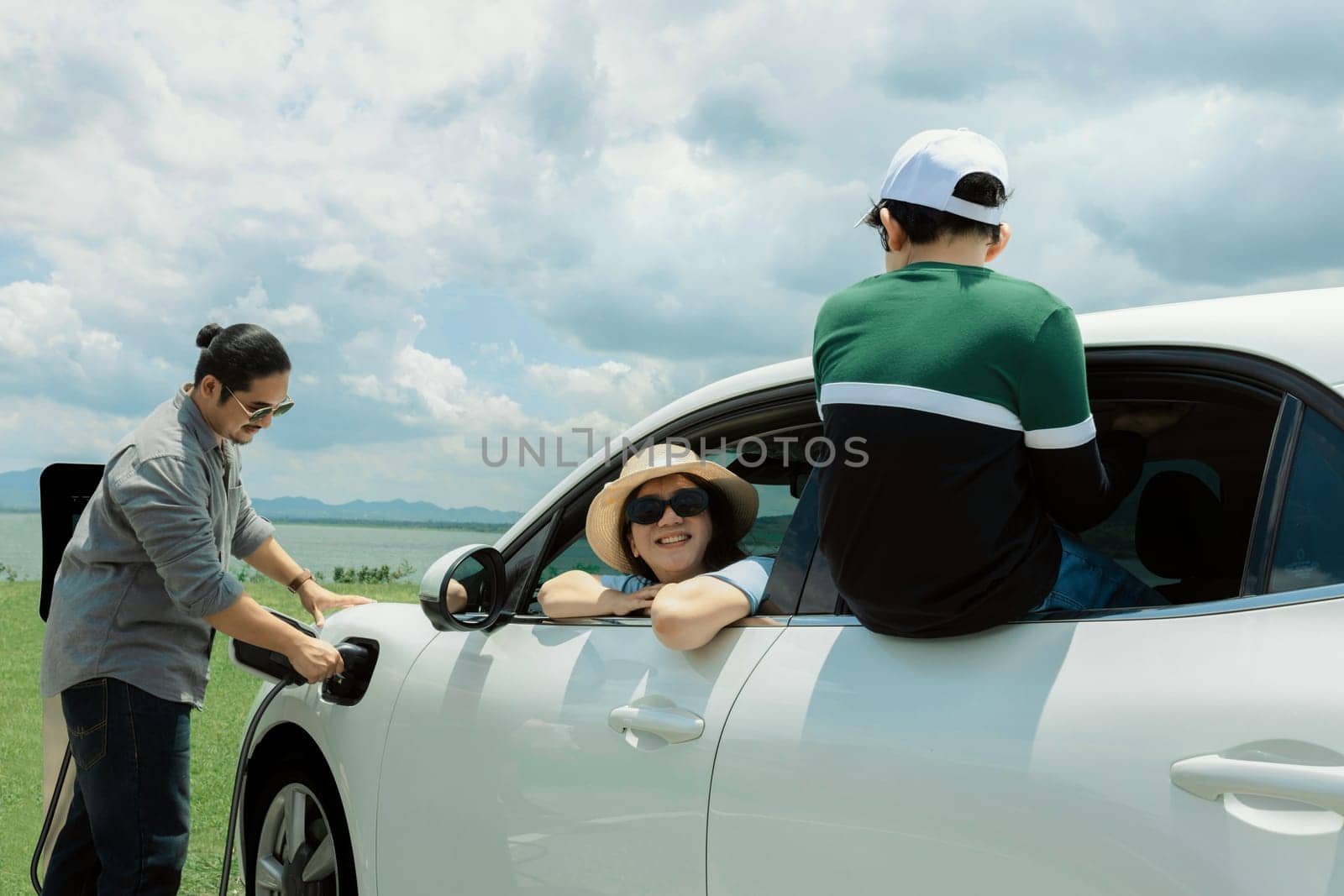 Concept of progressive happy family enjoying their time at green field and lake with electric vehicle. Electric vehicle driven by clean renewable from eco-friendly power sauce.