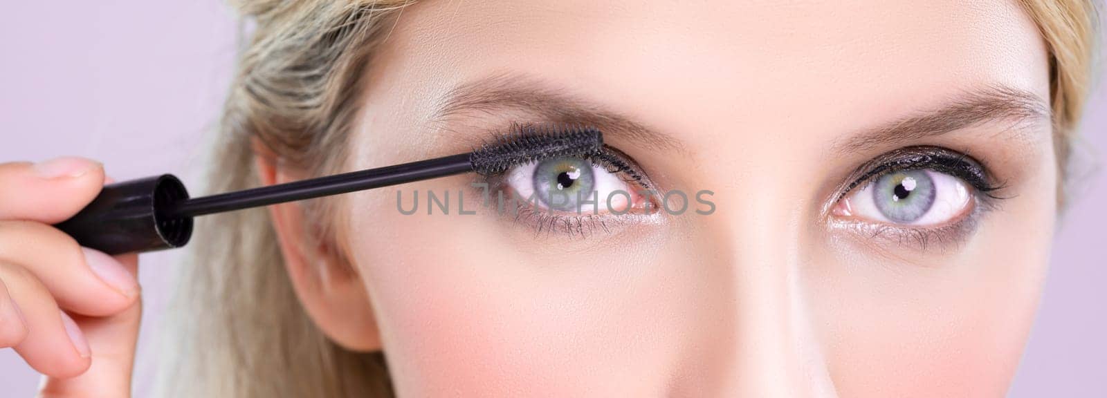 Closeup woman with blond hair putting alluring black mascara with brush in hand on long thick eyelash. Perfect fashionable cosmetic clean facial skin with beautiful eye young woman in high resolution.