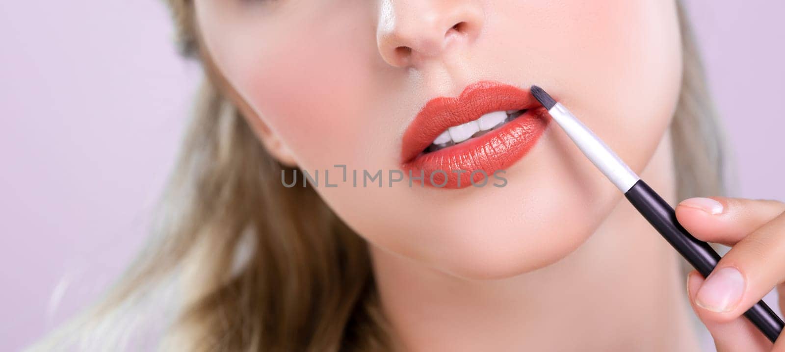 Closeup beautiful young woman putting alluring fashion glossy red lipstick. by biancoblue