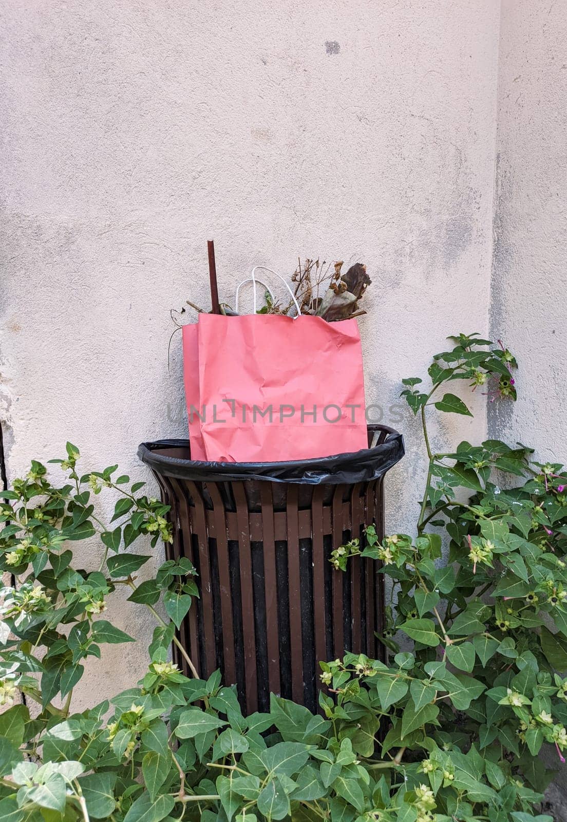 Luxury pink color bag in the trash bin on the street. France street luxury stylish paper bag with trash. Caring about nature, plastic pollution. High quality photo