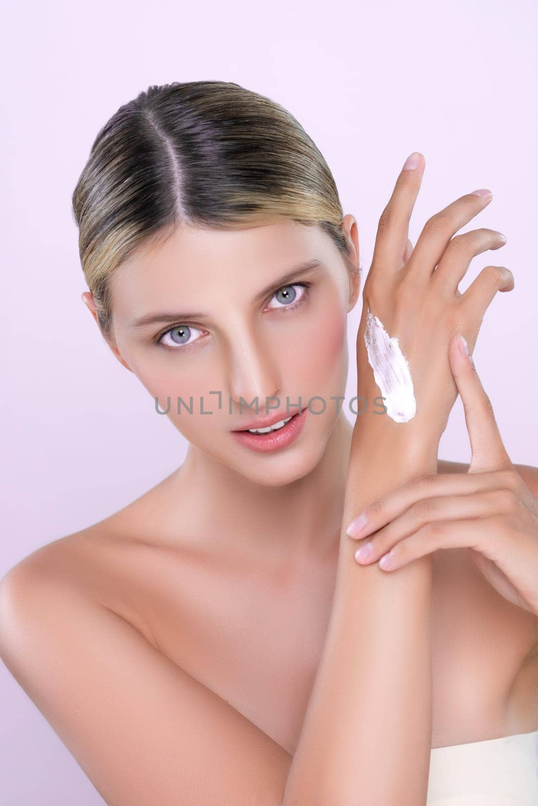Alluring beautiful woman applying moisturizer cream on her hand for perfect skincare treatment in pink isolated background. Caucasian women portrait with skin rejuvenation and cosmetology concept.