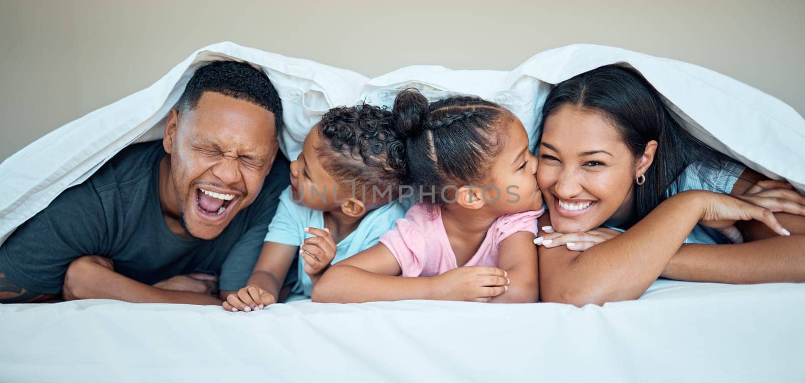 Black family, bed together and happy under blanket in home with love, care and bonding with kiss on cheek. Black woman, man and kids in bedroom in house for happy family moment, time or relax in home by YuriArcurs