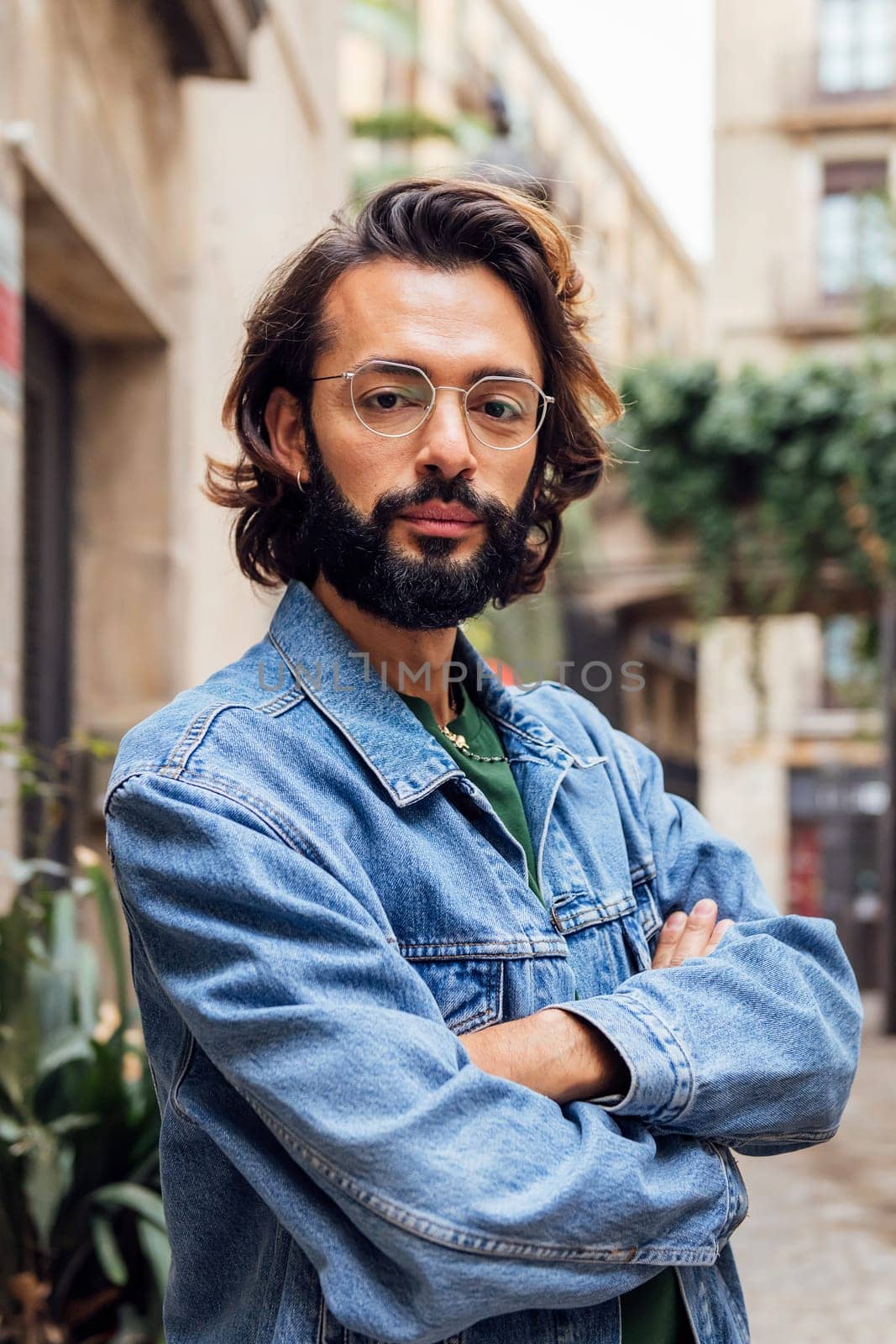 vertical portrait of a serious caucasian man with arms crossed in a nice old street with plants, concept of lifestyle and youth, copy space for text