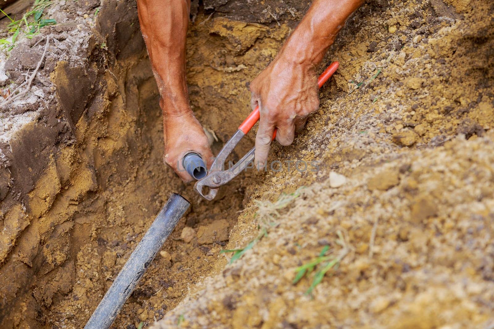 Installing an underground sprinkler system for watering the yard garden, a man works with pipes in the ground while installing the system by ungvar