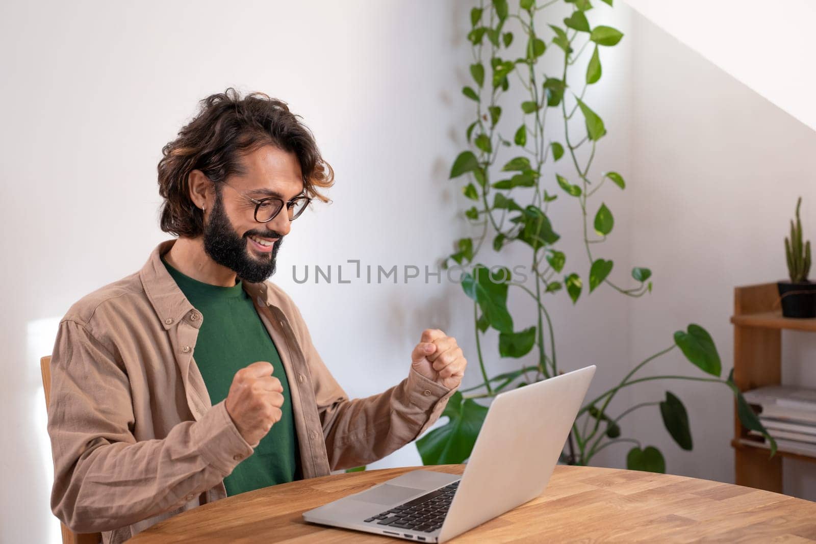 Cheerful man celebrates a success at work with his fists. Happy man reads good news in the laptop. by PaulCarr