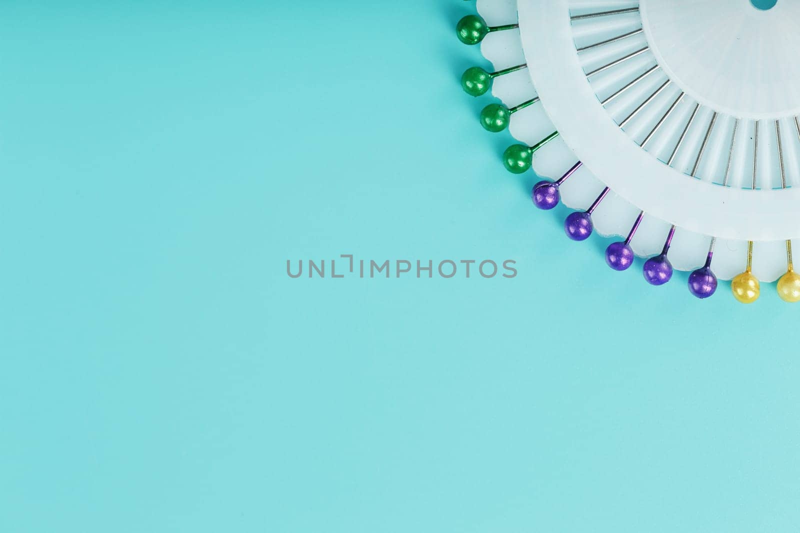 A set of multicolored needles pins in a round platform on a blue background with free space