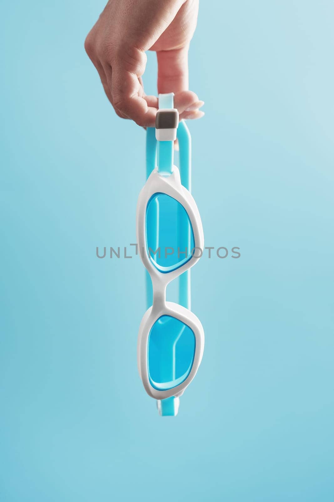 White swimming glasses in hand with a blue lens on a blue background by AlexGrec
