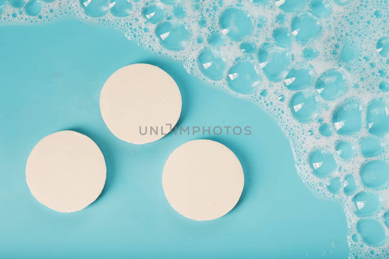 Three bars of round soap with foam on a blue background