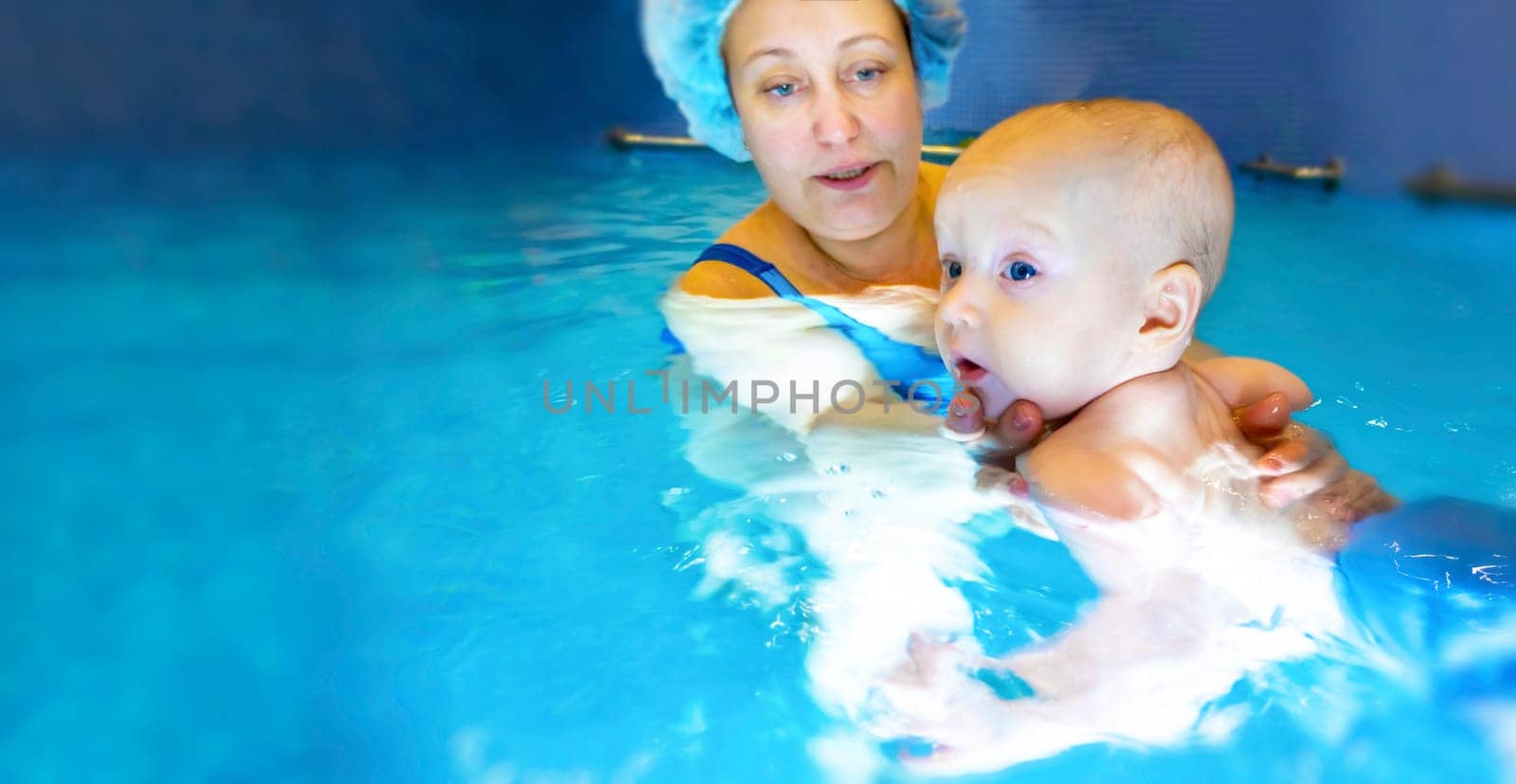 Adorable baby girl enjoying swimming in a pool with her mother early development class for infants teaching children to swim and dive. Swimming instructor doing exercises with a small child in the pool . banner with copy space