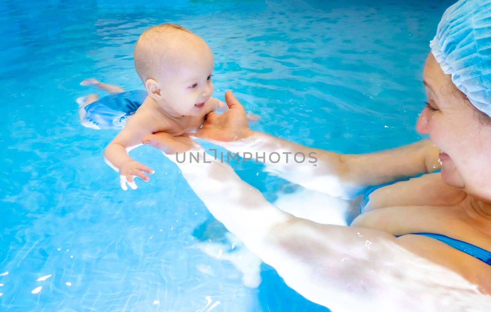 Adorable baby girl enjoying swimming in a pool with her mother early development class for infants teaching children to swim and dive. Swimming instructor doing exercises with a small child in the pool . High quality photo