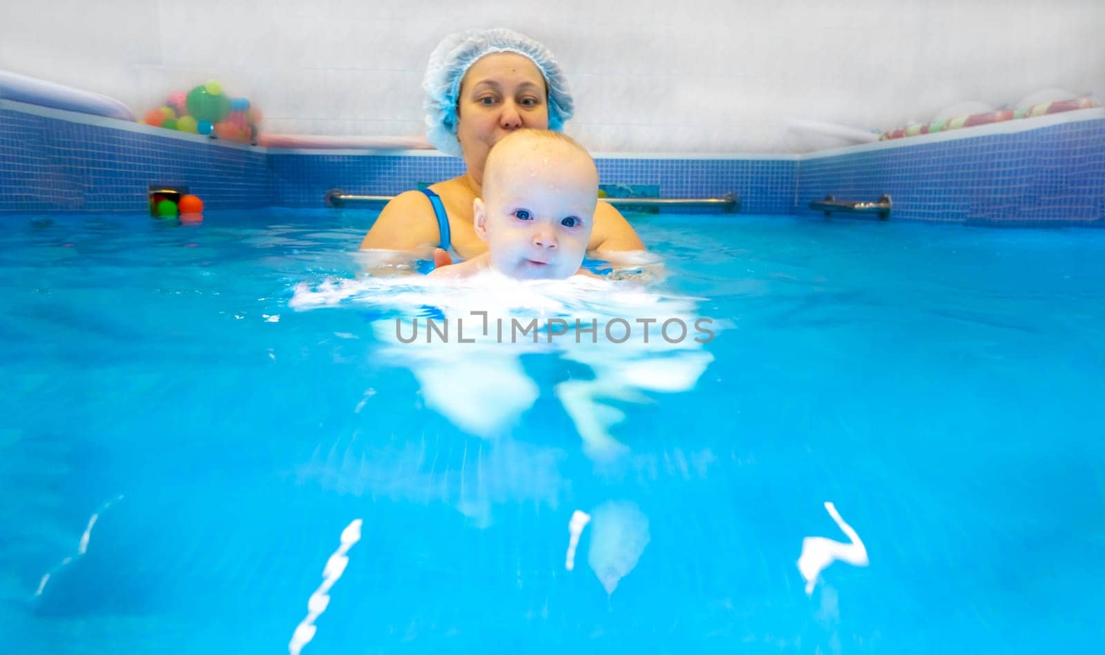 Adorable baby girl enjoying swimming in a pool with her mother early development class for infants teaching children to swim and dive. Swimming instructor doing exercises with a small child in the pool . High quality photo