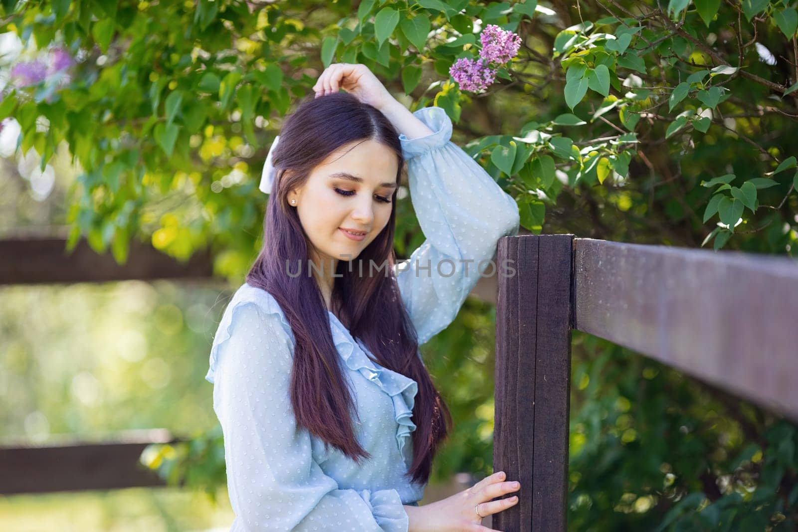 romantic beautiful girl with long hair , in light blue dress stands nearby fence, in the garden, in sunny day. Close up. copy space