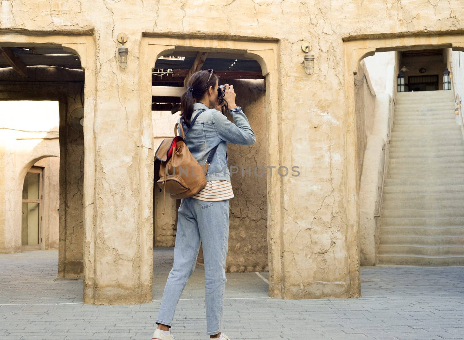 A young woman traveler with a backpack on her back walks and photographs the old narrow streets of Dubai Deira and Creek. Travel and sightseeing concept