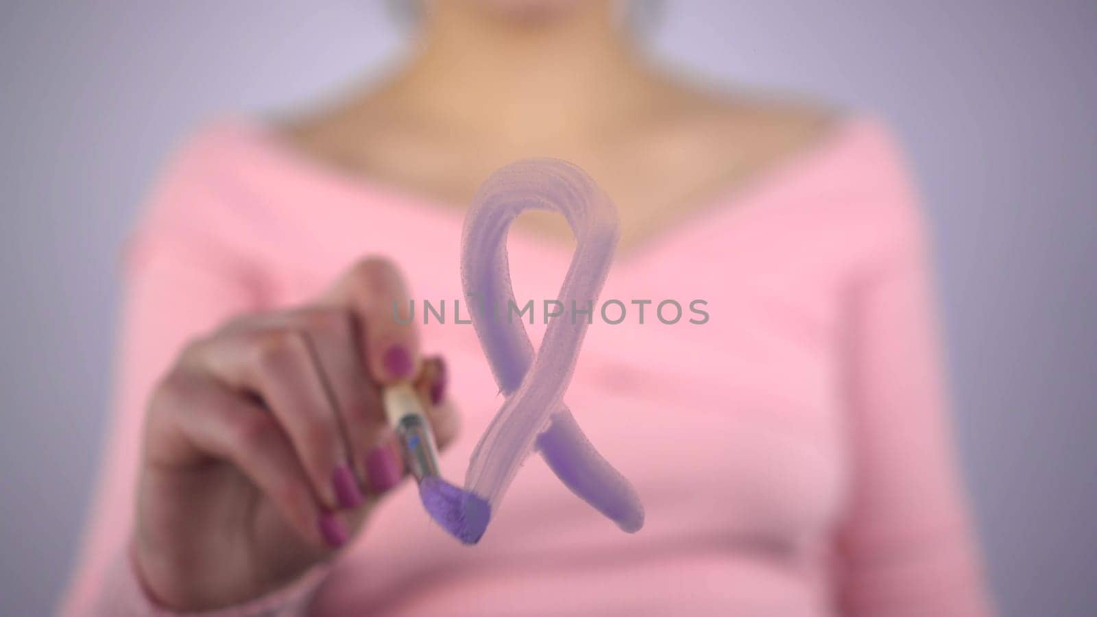 A woman draws a loop of lavender color on the glass, meaning all types of cancer. The girl draws with a brush on a transparent glass. 4k