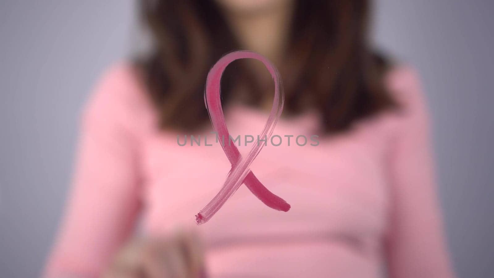 A young woman paints a breast cancer symbol on a glass. The girl draws a pink loop on the glass with a brush. 4k
