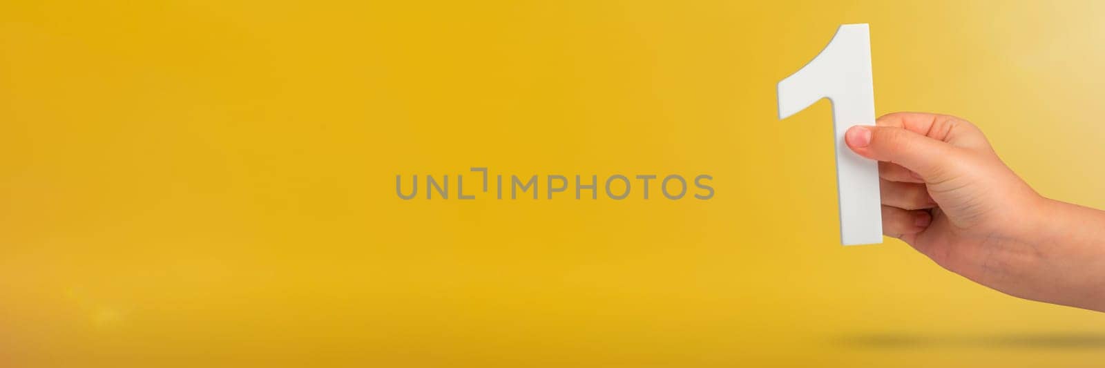 Number one in hand. A hand holds a white number one on a yellow background with copy space. Concept with number one. 1 percent rate, birthday, first or winner