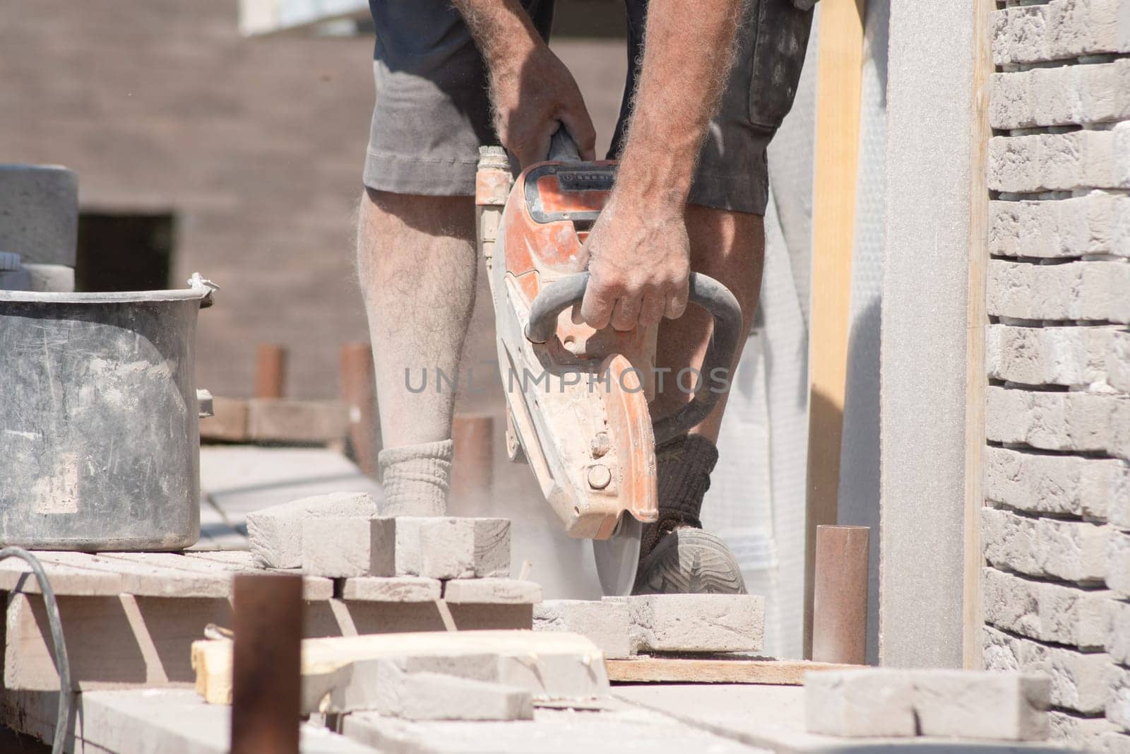 A gray-haired man saw bricks with a concrete saw of the right size for subsequent laying out in the facade of the house, High quality photo
