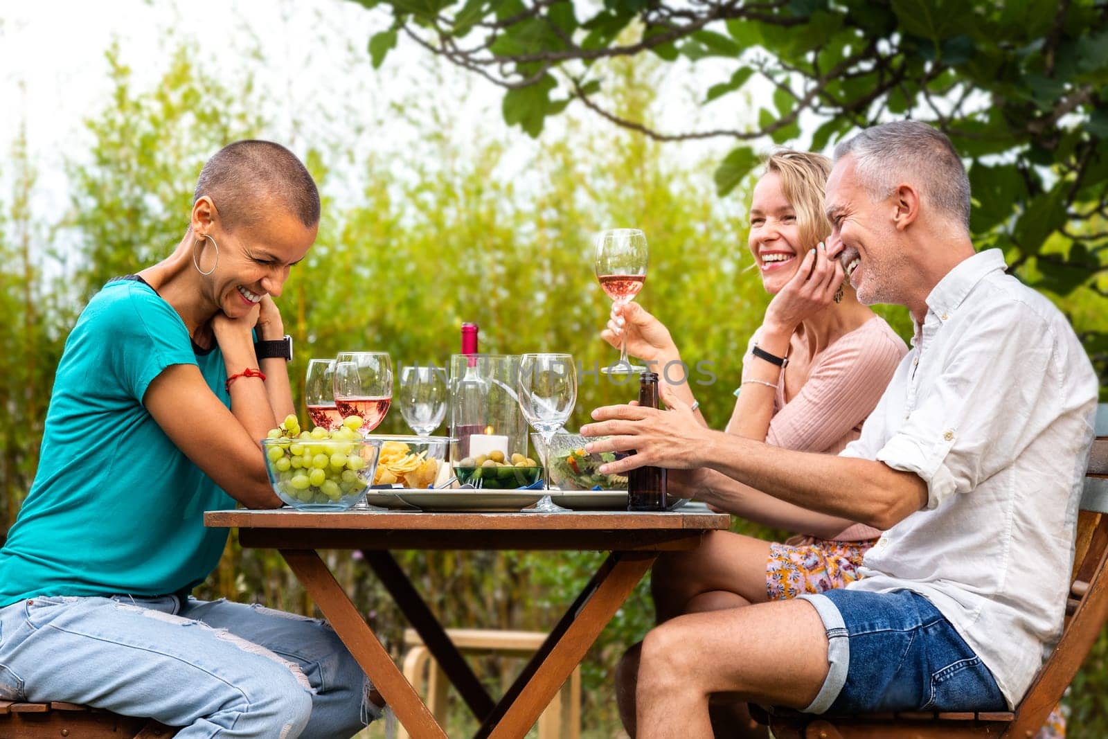 Group of friends laughing, talking and drinking wine during garden dinner party. by Hoverstock