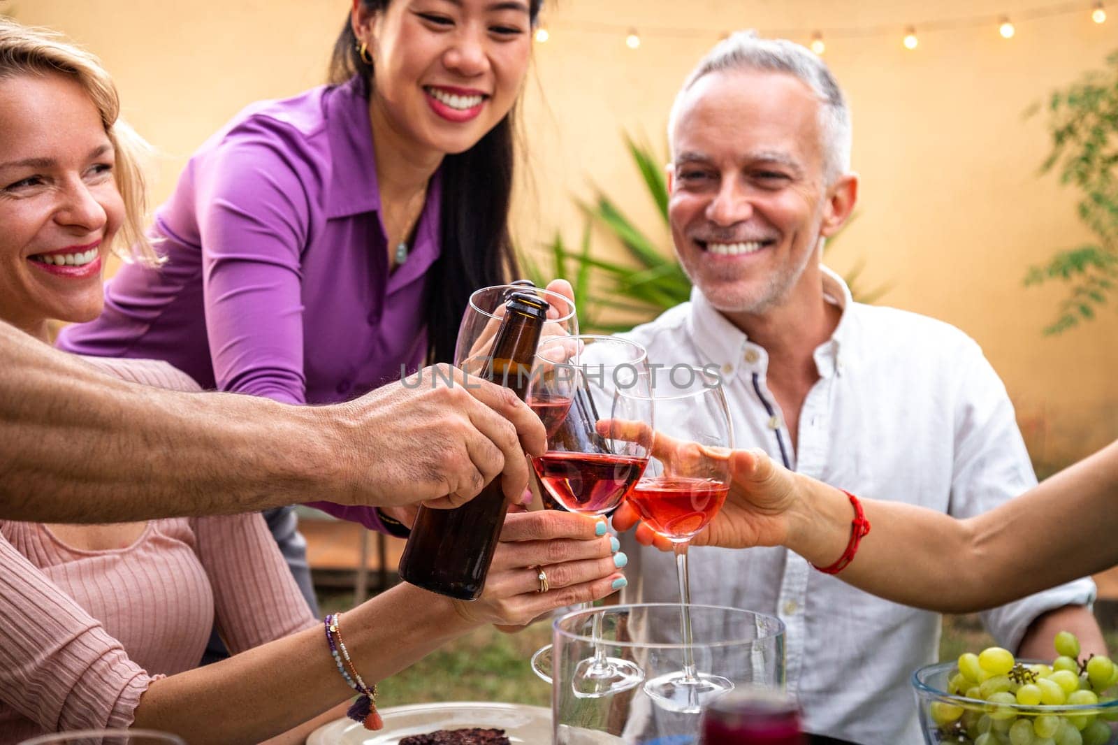 Close-up of diverse happy friends having fun, toasting with wine and beer during garden dinner party. by Hoverstock