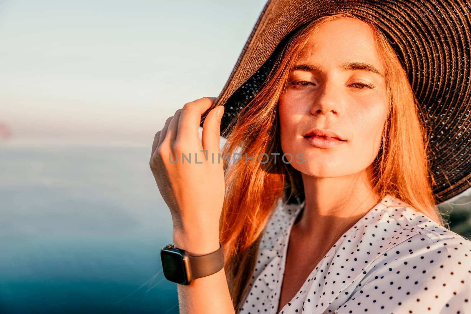 Portrait of happy young woman wearing summer black hat with large brim at beach on sunset. Closeup face of attractive girl with black straw hat. Happy young woman smiling and looking at camera at sea