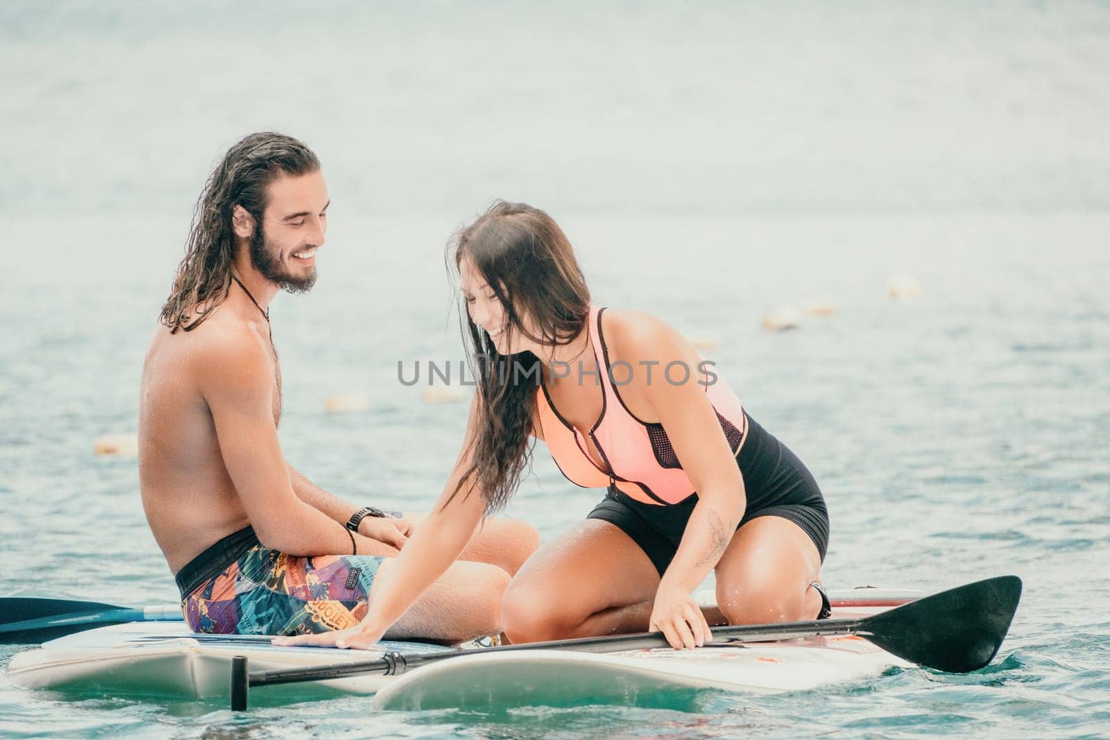 Sea woman and man on sup. Silhouette of happy young woman and man, surfing on SUP board, confident paddling through water surface. Idyllic sunset. Active lifestyle at sea or river