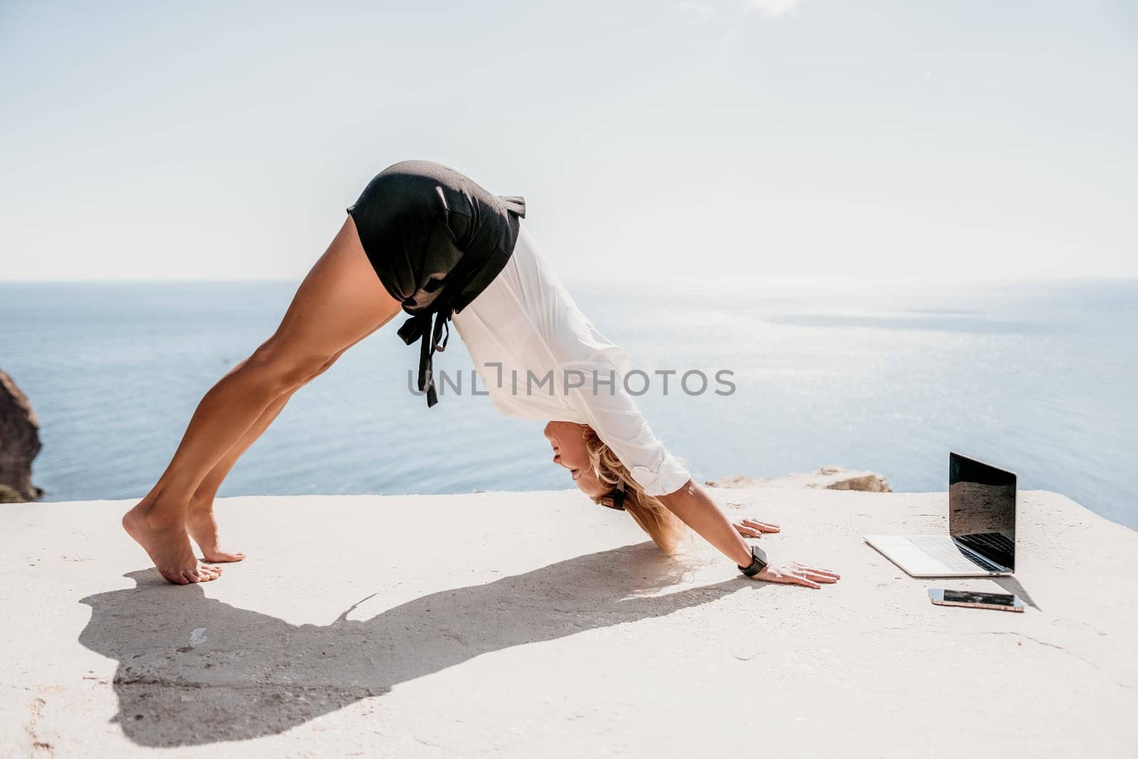 Happy girl doing yoga with laptop working at the beach. beautiful and calm business woman sitting with a laptop in a summer cafe in the lotus position meditating and relaxing. freelance girl remote work beach paradise