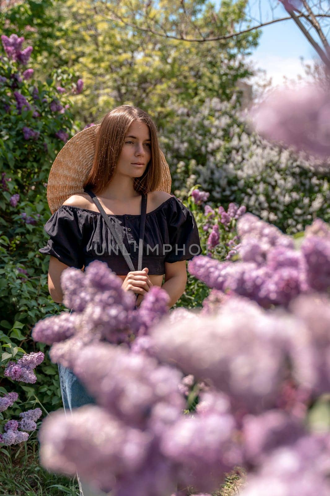 portrait of young woman with long hair outdoors in blooming lilac garden.