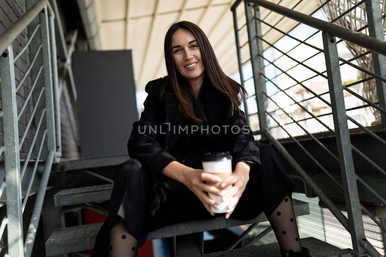 young adult brunette in a break from work drinking coffee on the stairs.