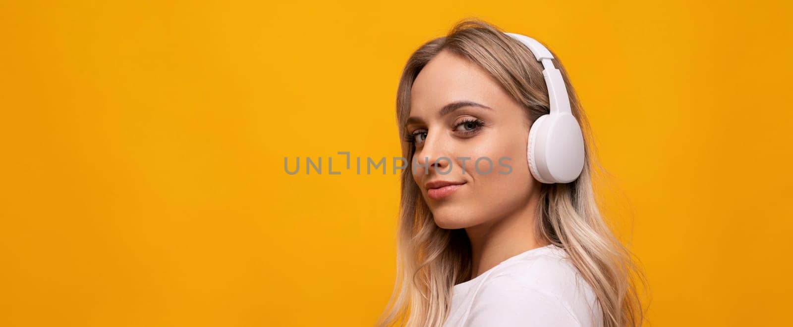 caucasian blonde woman posing in white headphones on orange background with empty space.
