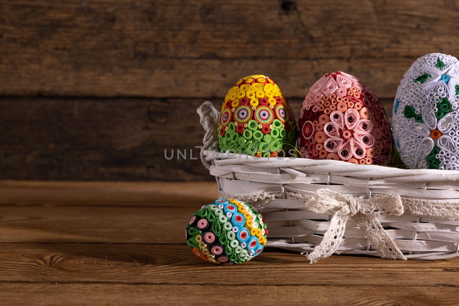 On a background of brown boards set a woven basket with colorful Easter eggs. Easter composition as decoration and symbol of the holiday.