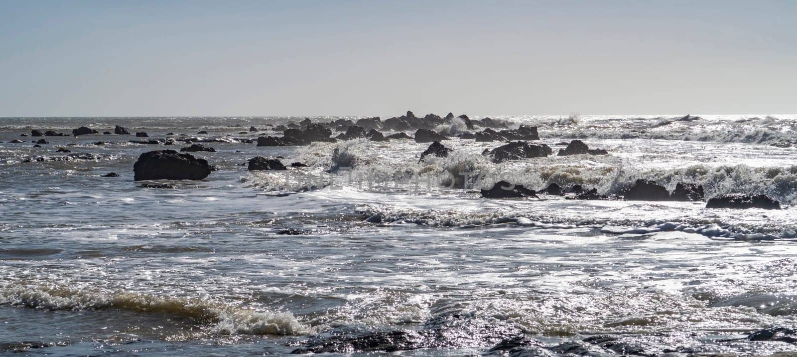 Blue sea and rocks storming. Wave spray over rocks. Rocky sea coast.