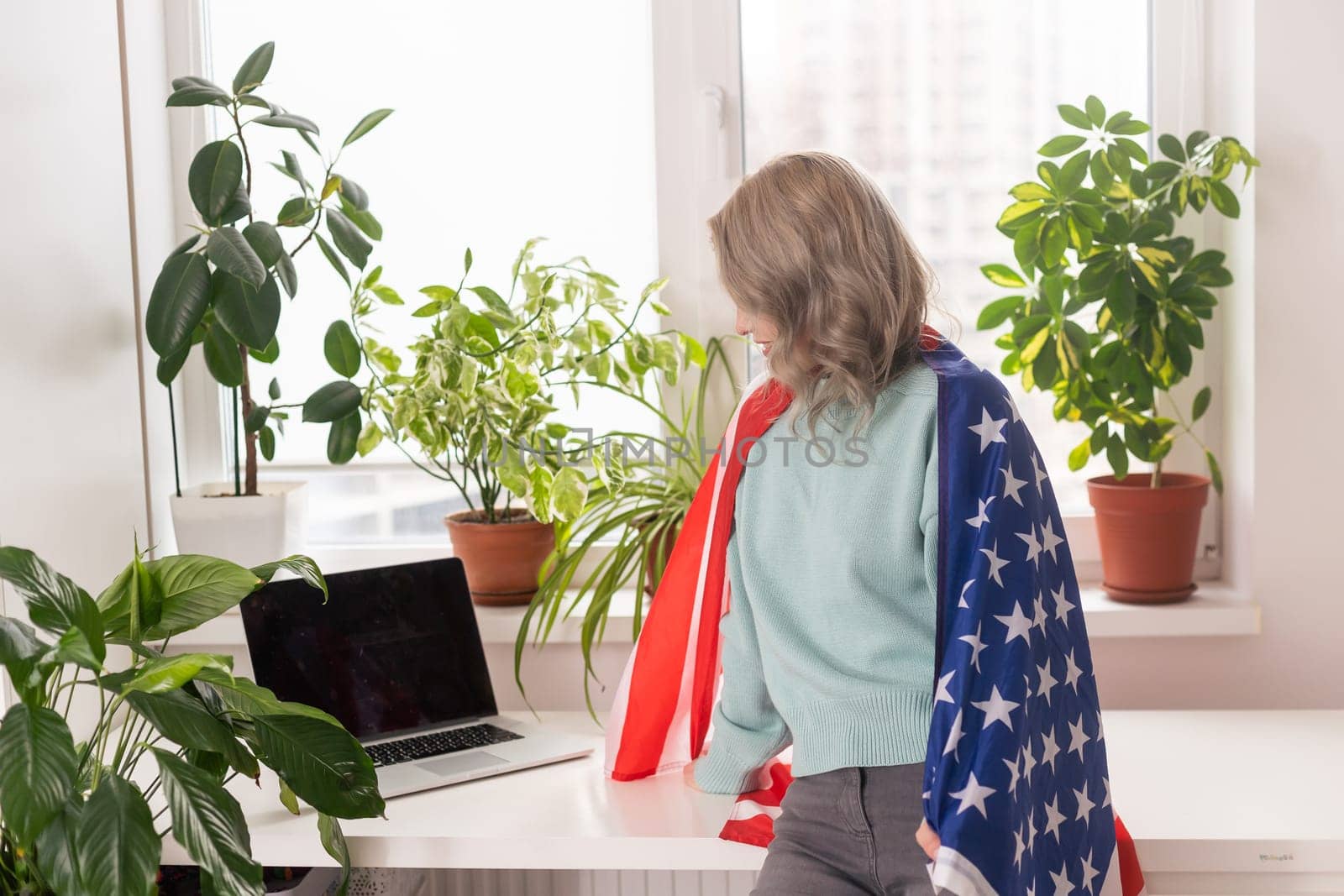 Picture of happy young lady with USA flag using laptop computer. Looking camera