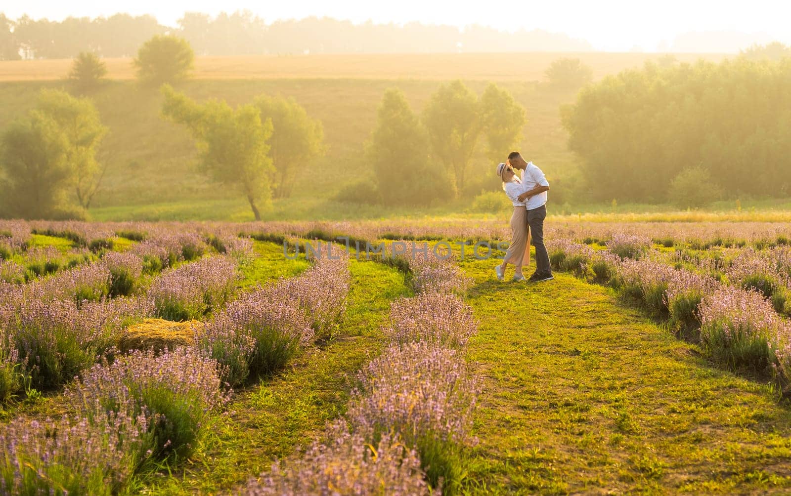 Smiling young couple embracing at the lavender field, holding hands, walking