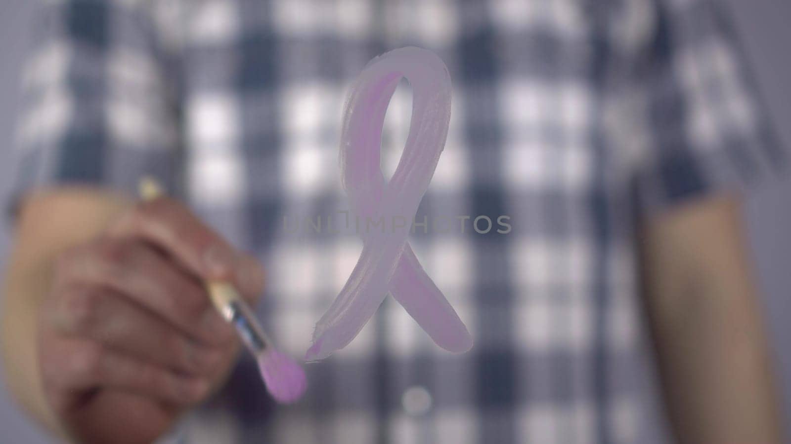 A man draws a lavender ribbon on glass in support of cancer patients. A young man paints with a brush the symbol of all types of cancer. Close-up. 4k