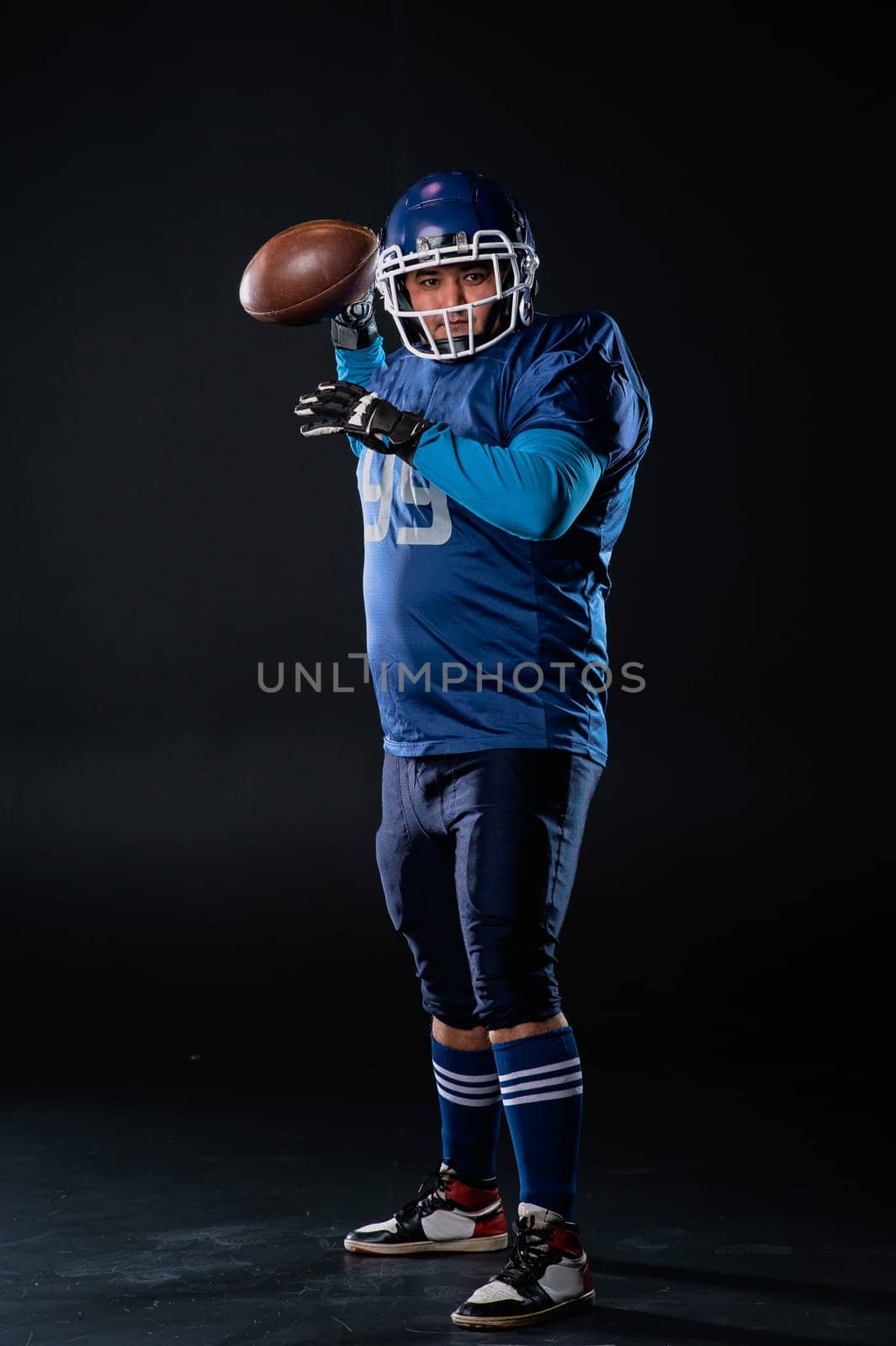 Portrait of a man in a blue uniform for american football throws the ball on a black background