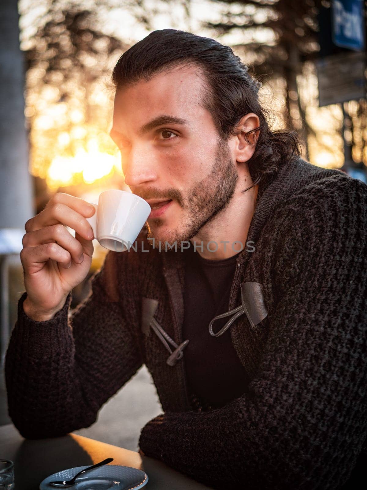 One handsome young man drinking espresso coffee, sitting outside in urban setting in European city