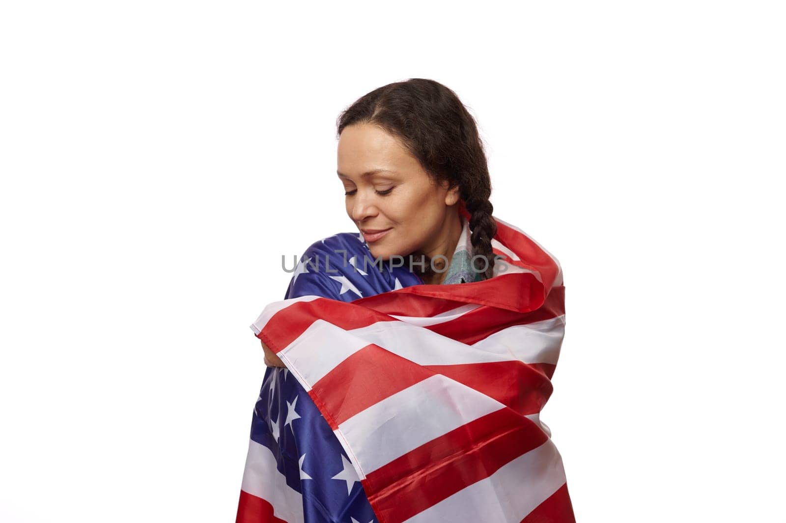 Isolated portrait on white background of a beautiful ethnic middle-aged woman, wrapped in US flag, proud to be american citizen, celebrating the independence day on July 4th. Copy advertising space