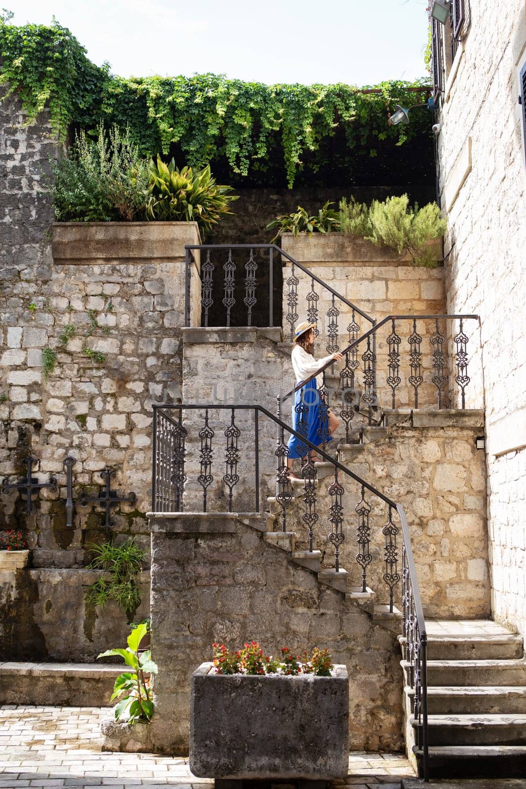 A girl in a blue dress and a straw hat walks the stairs in the old town of Kotor, Montenegro. by sfinks