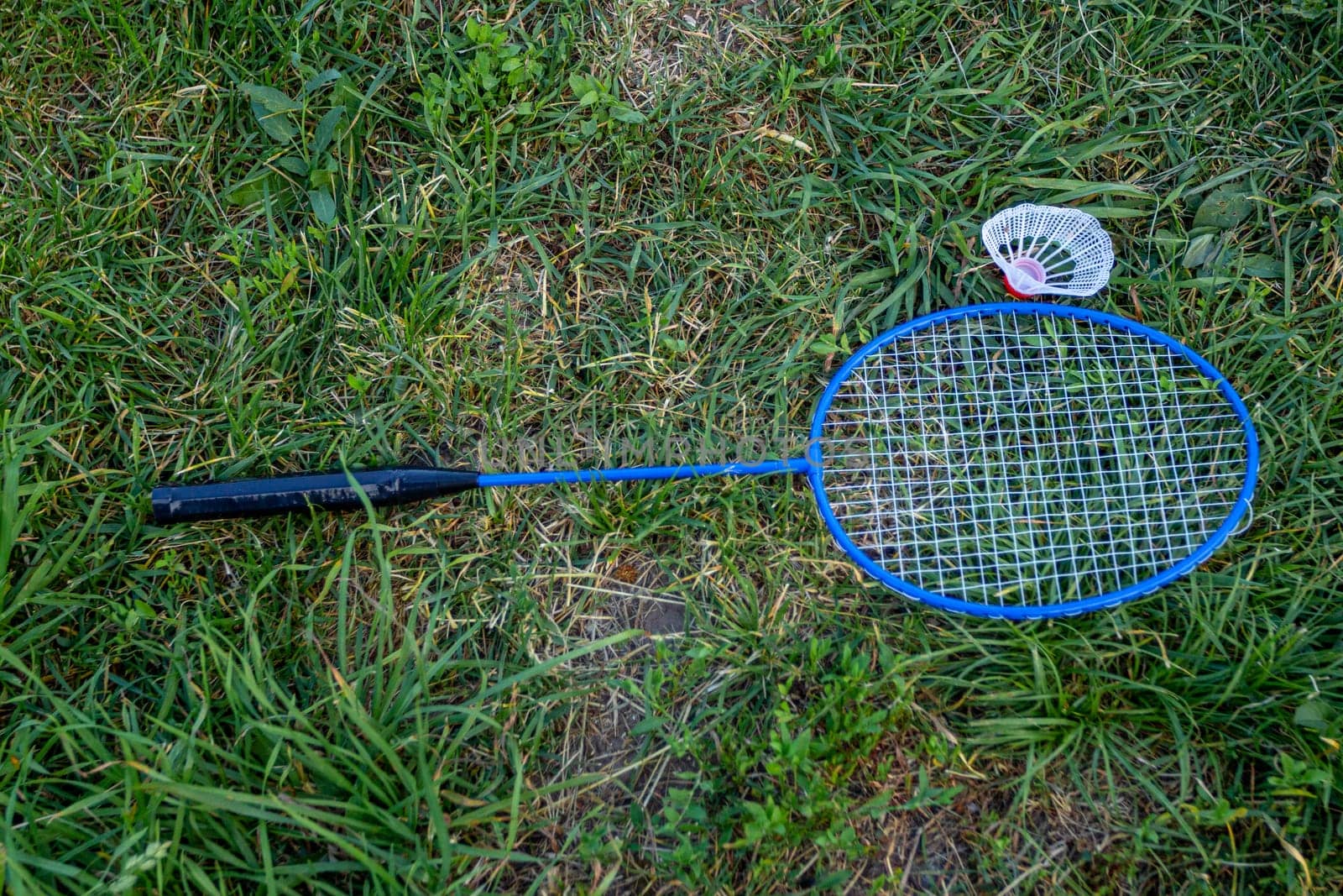 The badminton racket is lying on the green grass. Outdoor games. Sports equipment.